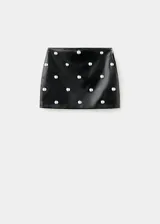 Minifalda de efecto piel en color negro, con corte recto y diseño adornado con tachuelas metálicas circulares distribuidas por toda la prenda. Cuenta con cierre de cremallera lateral y forro interior.
