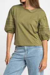 Remera de algodón color crudo con cuello redondo y mangas abullonadas de largo 3/4. Las mangas presentan detalles de encaje bordado y perforado con terminación elástica.