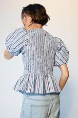 Top de cuello redondo con cuerpo de nido de abeja elástico y mangas globo con elástico en los puños. Presenta un diseño a rayas verticales en tonos azul, blanco y granate, con un bajo estilo peplum.