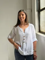 Blusa blanca de lino, con escote en V y tres botones frontales grandes de madera. Cuenta con mangas tres cuartos con presilla y botón para arremangar.