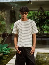 Remera de tejido de punto abierto, color crudo y beige, con diseño de rayas horizontales finas. Presenta cuello redondo y mangas cortas.