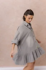 Vestido camisero corto de denim liviano azul con efecto desgastado, de corte oversize, con cuello camisero, botonadura frontal, bolsillo plaqué en el pecho, mangas largas y volado fruncido en el ruedo.