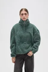 Buzo de textura afelpada con diseño a rayas horizontales en tonos verde y blanco. Presenta cuello alto con cierre frontal parcial y mangas largas holgadas.