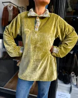 Buzo de plush color verde pistacho con cuello tipo camisa y puños en tela de paño estampada a cuadros. Presenta cierre frontal parcial con botones de madera y mangas largas.
