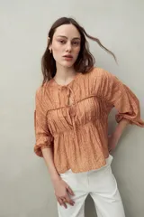 Blusa estampada de caída fluida con cuello redondo y lazos frontales, diseño con cortes horizontales y frunces, mangas largas con puños elastizados.