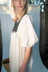Túnica de lino color beige, de corte midi y diseño holgado, con mangas cortas y pechera combinada con tela estampada y detalles de flecos y botones.