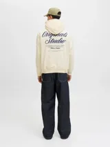 Buzo con capucha de calce holgado, color crema, confeccionado en tejido loopback con interior levemente afelpado. Presenta bolsillo frontal tipo canguro, puños y ruedo acanalados, y estampado con texto en el pecho.