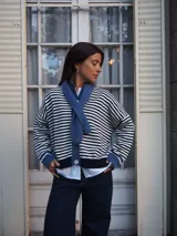 Sweater de punto a rayas horizontales blancas y azul marino, con cuello redondo, cierre frontal con botones y mangas largas con puños y detalles en tono azul.
