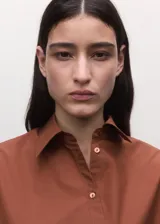 Camisa marrón de algodón con diseño cruzado, cierre lateral con lazo, cuello camisero y manga larga.