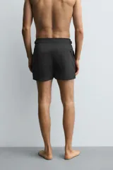 Bañador de hombre color negro, de largo medio, confeccionado en tejido técnico. Presenta cintura elástica ajustable con cordón interior, trabillas laterales, bolsillos frontales y bolsillo trasero con cierre de cremallera.