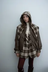 Chaqueta de cuero sintético color marrón con capucha y solapas amplias en tela escocesa a cuadros. Posee cierre frontal, puños elásticos y diseño de corte holgado.
