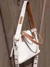 Cartera bandolera de cuero color crema con doble asa de mano marrón y correa larga de cinta con logo.