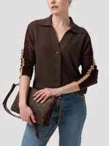 Sweater de punto color marrón con cuello camisero y cierre frontal de botones. Presenta detalles de tejido calado en las mangas con franjas laterales en contraste y terminaciones en crochet en el cuello y la tapeta.