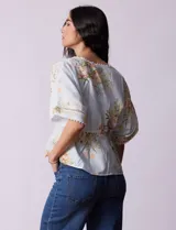 Blusa blanca estampada con flores azules, escote en V y mangas cortas amplias. Detalles de puntilla en escote y mangas.