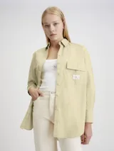 Camisa de estilo utility con corte oversized y largo, confeccionada en algodón. Presenta cuello en punta, cierre frontal de botones, bolsillo de parche en el pecho con insignia de la marca y bajo redondeado.