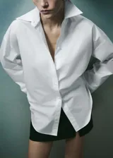 Camisa blanca de popelina de algodón, corte amplio, cuello camisero clásico y cierre frontal con botones.