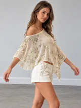 Top beige semitransparente con diseño de un solo hombro, mangas amplias y bordados metalizados con lentejuelas.