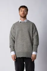 Sweater oversize de tejido de punto en color gris, con cuello redondo, puños y ruedo acanalados con detalles de desgaste. Presenta un diseño minimalista con logo tejido en la espalda.