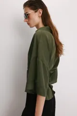 Camisa de corte holgado en color beige, con cuello solapa, escote en pico y mangas cortas amplias. Presenta cierre frontal con botones a tono.