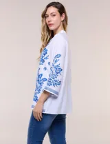 Blusa blanca con bordados florales en azul, de manga tres cuartos y cuello mao con escote en V.