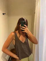 Blusa de tejido de punto con acabado brillante, escote en V profundo y espalda abierta. Presenta un diseño holgado y sin mangas.