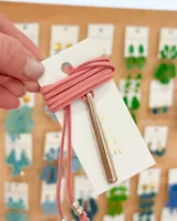 Gargantilla tipo choker con tira de gamuza sintética color rosa viejo, dije metálico tubular dorado y cuentas plateadas.