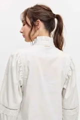 Camisa de manga larga color marrón, con cuello alto con volados, botonadura frontal y detalles calados en las mangas abullonadas.