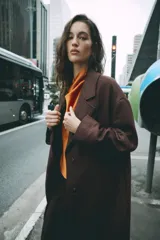 Abrigo largo de Zara confeccionado en hilatura con lana, de color marrón oscuro. Cuenta con cuello solapa, manga larga, bolsillos de vivo en el delantero y cierre frontal con dos botones.