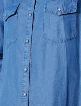 Camisa de manga larga en tela denim de color azul medio, con cuello clásico, botones frontales y dos bolsillos de parche con solapa en el pecho.
