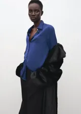 Camisa de satén azul satinado con cuello camisero, manga larga y cierre frontal de botones.