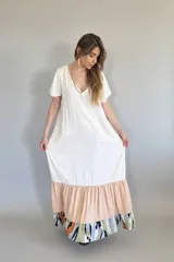 Vestido largo de manga corta con cuello en V, de color crema liso en la parte superior. La falda es de corte amplio con un volante en color melocotón liso, y un volante inferior con estampado abstracto en tonos verde oliva, negro, naranja y azul claro.