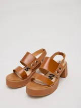 Sandalias de plataforma con taco cuadrado de 6 cm y base de 3 cm. Presentan dos tiras anchas en el empeine con detalles de doble argolla metálica en los laterales y una correa trasera con elástico para mayor ajuste.