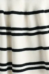 Saco ajustado en punto fino suave, de color blanco con rayas negras, cuello redondo, manga japonesa, botones hasta la cintura y peplum acampanado.