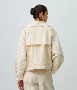 Tapado corto tipo trench coat confeccionado en sarga de algodón, de color beige con estampa de rayas finas verticales y horizontales. Presenta cuello solapa, mangas largas, bolsillos laterales con ribete y cierre frontal cruzado con doble botonadura.