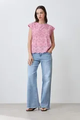 Blusa de algodón color rosa pastel con frente de tela broderie, cuello redondo y mangas cortas con terminación al corte.