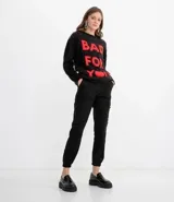 Buzo de tejido peluche negro con cuello redondo y manga larga. Presenta un estampado frontal en rojo que dice "BAD FOR YOU", donde la palabra "YOU" está reemplazada por un corazón.