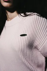Sweater de punto acanalado color rosa, de manga larga, con cuello redondo y detalle de logo metálico en el pecho.