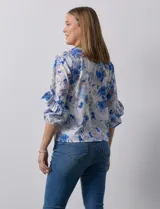 Blusa de gasa estampada con flores azules y violetas sobre fondo blanco, de manga 3/4 con volados.
