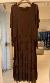 Vestido largo color marrón, sin mangas, con diseño escalonado de múltiples volados con terminaciones deshilachadas y silueta fluida.