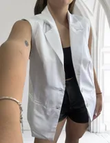 Chaleco largo blanco de corte sastrero con solapas, sin mangas y con cierre de dos botones.