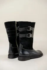 Bota de caña media combinada en cuero liso y gamuza, color negro. Presenta un diseño con doble hebilla lateral metálica y cierre de cremallera vertical en el lateral interno. Cuenta con suela plana y tacón bajo.