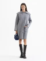 Tapado de tejido de punto color gris, con cuello tipo solapa grande, cierre frontal con botones a presión y bolsillos frontales. Presenta costuras decorativas visibles y diseño de largo medio.