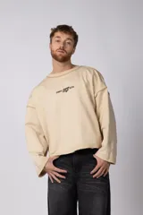 Buzo de cuello redondo confeccionado en tejido rústico con bordes al corte y costuras expuestas. Presenta un diseño boxy con estampado frontal y es reversible, permitiendo su uso por ambos lados.