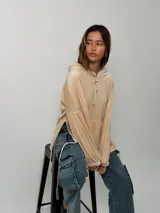 Canguro de plush color beige con capucha, bolsillo frontal tipo canguro, mangas globo con puños fruncidos y tajos laterales con tiras ajustables.