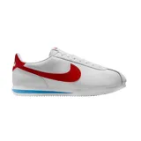 Championes Nike modelo Cortez, de diseño clásico en color blanco con el logo de la marca en rojo vibrante en los laterales y talón. Presenta una entresuela con una franja azul distintiva y suela dentada para mayor tracción.