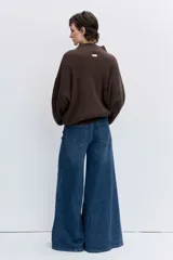 Jersey de punto color marrón chocolate, de cuello alto y corte holgado. Presenta un diseño acanalado y un detalle de costura decorativa en color blanco que recorre la parte superior de las mangas.