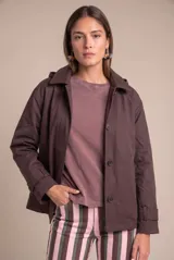 Trench oversize de color marrón, confeccionado en mezcla de algodón y poliéster, con cuello camisero, cierre frontal con botones y mangas largas con trabillas ajustables en los puños.