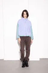 Camisa corta con cuerpo a rayas verticales azules y blancas, mangas a rayas verticales verdes y blancas, cuello camisero y cierre frontal con botones dorados.