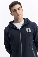 Campera con capucha de algodón y poliéster, color blanco, con cierre frontal negro y cordones negros en la capucha. Presenta un pequeño parche cuadrado negro con texto blanco en el pecho izquierdo y cierres negros en los bolsillos laterales.