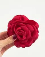 Broche decorativo con forma de flor de tela roja, con pétalos superpuestos que simulan una rosa o camelia.